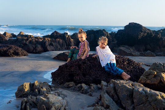 Two young hippie girls posing at the rocky ocean beach.