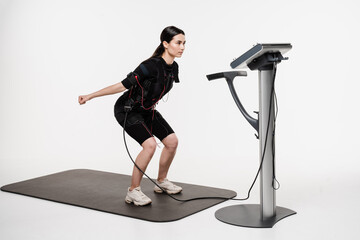 Fitness girl in EMS suit is doing workout sport training that uses electrical impulses to stimulate...