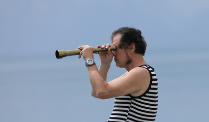old sailor with a spyglass on the sea - obrazy, fototapety, plakaty