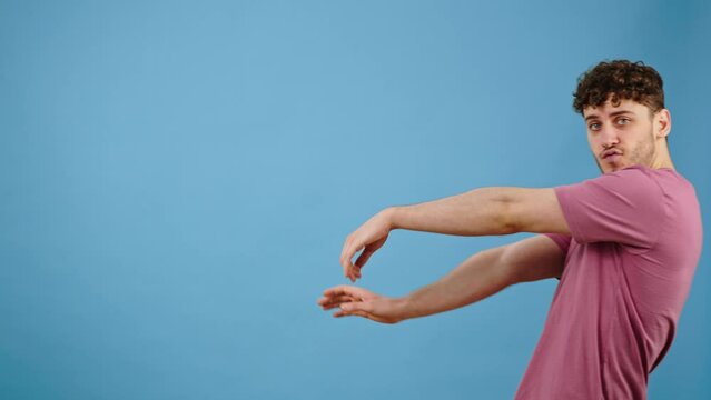 Handsome man appears over blue background, performing freestyle dance and wainks looking at camera