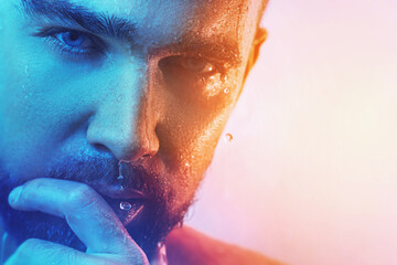 Handsome young man with wet face in blue and orange light
