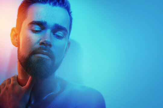 Handsome young man with wet face in blue and orange light