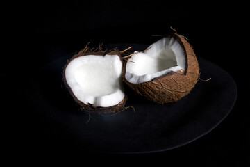 Closeup photo of broken in halves coconut against black background. 