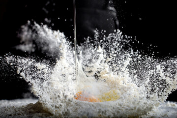 Close up view of yolk falling on flour on black background  - Powered by Adobe