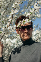 Man standing near blooming tree with white flowers in spring garden and looking away 