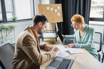 stylish business partners working with documents near laptops in office.