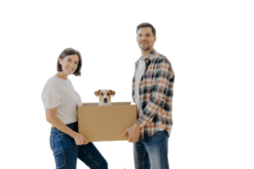 Happy family couple hold carton box with small puppy, stand indoor against big window, glad to become homeowners, unpack things in own apartment, looks gladfully at camera. Family moving day