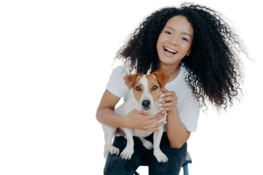 Portrait of joyful curly girl petting her dog, rejoicing buying jack russell terrier, smiles broadly, plays with animal, wears casual clothing, isolated over white background, enjoys good day