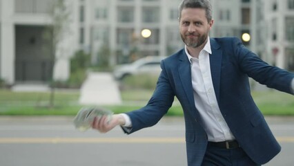 Business man hold money outdoor. Rich man in suit with money dollar bills. Successful businessman with dollar banknotes. Slow motion. Rich millionaire in suit holding money. - Powered by Adobe