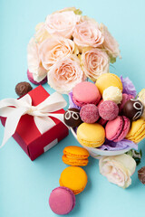 Macaroons, Gift Box, Rose Flowers and Chocolate Candies on Blue Background. Spring Presents Concept