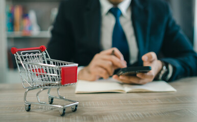 Business man wearing suit and calculates the budget. Shopping cart a on table with mobile. Budget...