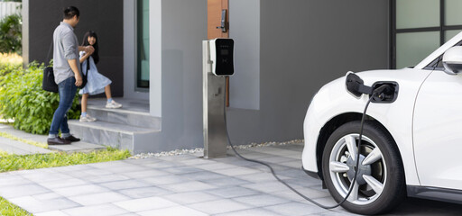 Progressive father and daughter plugs EV charger from home charging station to electric vehicle....