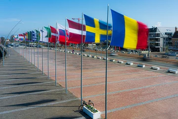 Fotobehang Inernational flags waving in the sky at the belgium coast city Nieuwpoort.  Flags at the belgium coast north sea waving in the wind with a blue sky.  Flags in movement, in flanders, west-vlaanderen. © robin