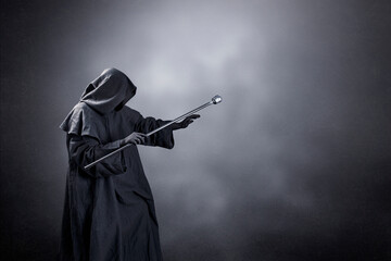 Wizard with hooded cape and magic staff over dark misty background