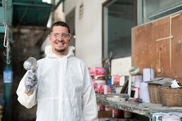 Portrait of automobile repairman painter in protective workwear holding spray gun and airbrush at...