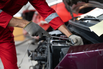 Mechanic man hands using spanner tighten car battery at auto car garage service. Car repair and maintenance concept.