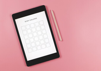 flat lay of digital tablet with template 30 day challenge on screen,  pink stylus pen,   isolated on pink background.