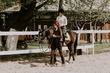 A woman instructor teaching girl how to ride a horse.  Female rider practicing on a horseback learning equestrian sport. Active lifestyle and leisure activity concep