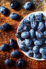 Fresh black plums on a white plate against dark orange background. Top view