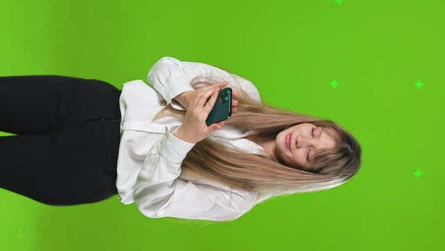 Smiling young woman with long hair using smartphone in studio. Front view of attractive female student browsing internet with mobile phone, in slow motion, horizontal. Concept of lifestyle.