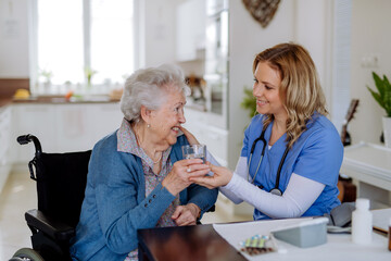 Nurse giving medicine to senior woman at her home.
