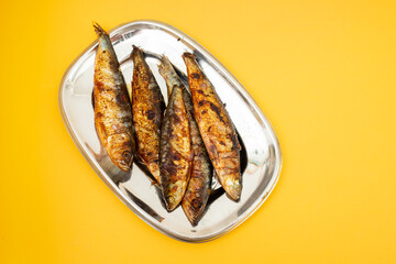 Grilled sardines in metal dish on yellow