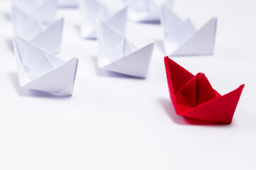 High angle close up shot of a red paper boat followed by many white boats.