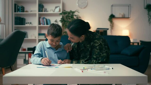 Female service member and her cute son drawing together at home, family reunion