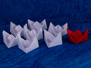 White and red paper boats on blue textured paper as high tides of sea in leadership concept.