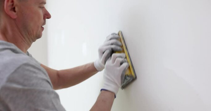 Builder putty and plasterer cleans white wall in room. Builder working inside house