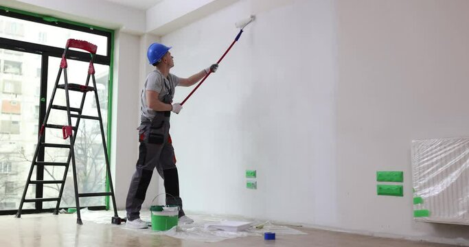 House painter paints wall white with roller. Painting walls or ceiling in apartment