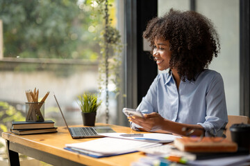 African American woman sitting in front of a laptop and holding a mobile phone