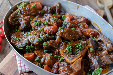 Osso bucco or osso buco, braised beef shanks in old fashioned roasting pan on wooden background