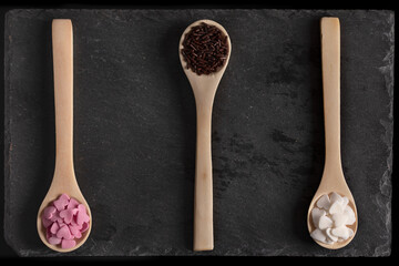 three wooden spoons filled with pink and white sugar hearts and chocolate noodles