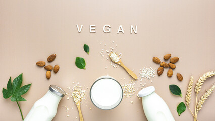 Pflanzliche Milch Alternativen in Glasflaschen und Zutaten auf einem beigen Hintergrund. Flat lay, Vegan.