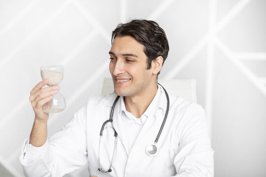 Close-up photo of smiling physician holding hourglass. Time and health concept	
