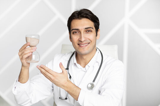 Close-up photo of smiling physician holding hourglass. Time and health concept	
