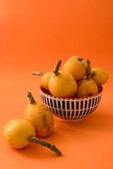 Fruit still life with ripe medlars in a bowl on an orange background and copy space
