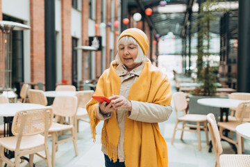 Portrait of old Woman in yellow hat using Phone and standing outdoors. Phone Communication. Happy cheerful senior women walking on city street, Urban lifestyle concept. Traveler