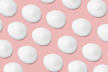 Lots of smears of cosmetic cream. Light, smooth surface. Texture of spreadable cream. Liquid creamy strokes. On a pink background. Cosmetic background, banner.