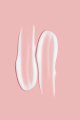 Lots of smears of cosmetic cream. Light, smooth surface. Texture of spreadable cream. Liquid creamy strokes. On a pink background. Cosmetic background, banner.