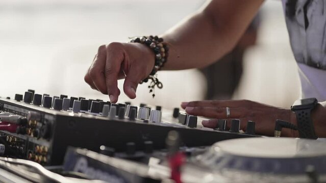 DJ handling controller close up with hands moving outdoors in the day light at sunset near the beach wearing bracelets and a smart watch
