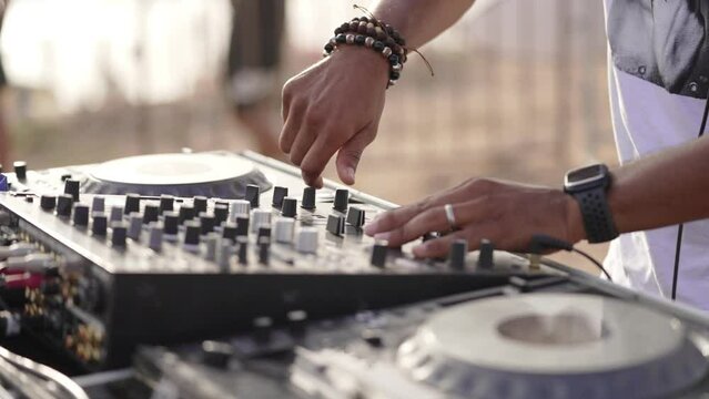 DJ handling controller close up with hands moving outdoors in the day light at sunset near the beach wearing bracelets and a smart watch
