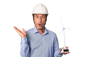 A middle-aged architect man holding a windmill model surprised and shocked.