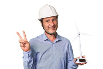A middle-aged architect man holding a windmill model joyful and carefree showing a peace symbol with fingers.