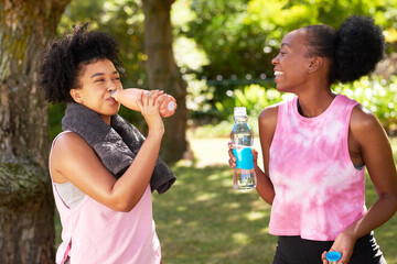 Two young Black friends drink water and chat after yoga session in the park