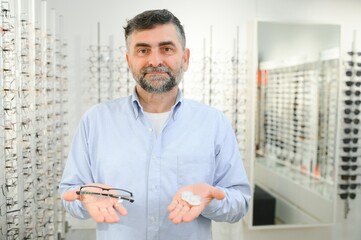 Ophthalmology Concept. Portrait of man choosing between eyeglasses and contact lenses standing in...