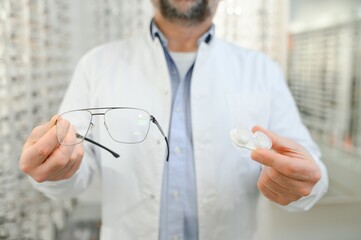 Male doctor holding contact lens case and glasses, indoors.