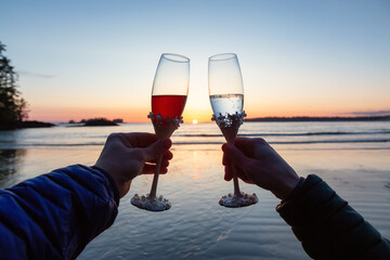 Man and Woman Cheers with Champagne Flute Glasses on the Beach at Sunset. Tofino, Vancouver Island, British Columbia, Canada.