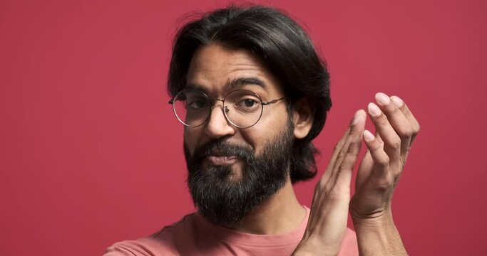 Closeup portrait of happy young man with beard and eyeglasses shaking head and clapping hands against red background